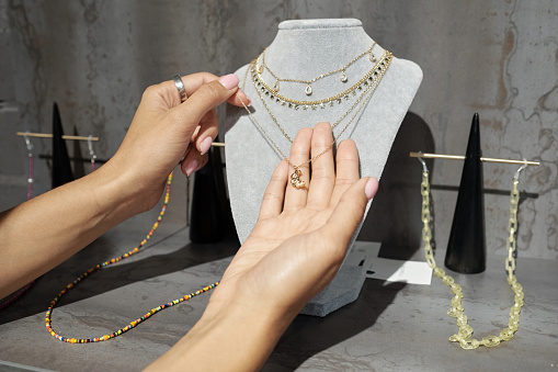 Hands of young female consumer holding golden chain with pendant hanging on grey velvet holder on display