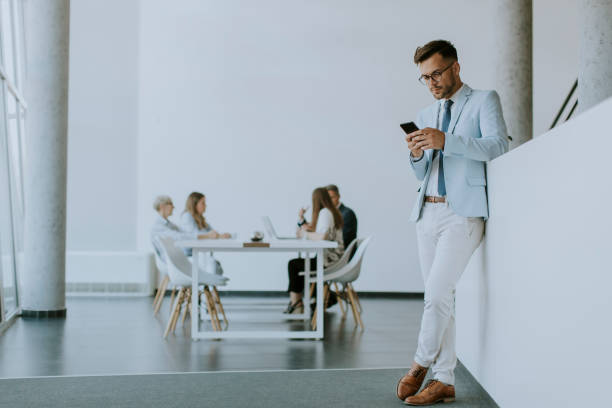 istock Young man using his mobile phone while his colleagues working in the background 1358416773