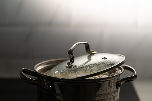 A saucepan on the stove in the kitchen. Boiling bubbling water while cooking. Boiled potatoes, vegetables or soup. The dishes are covered with a lid.