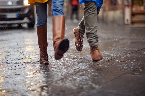Close-up of a young couple and their legs how walking on the rain in the city in a hurry manner. Walk, rain, city, relationship