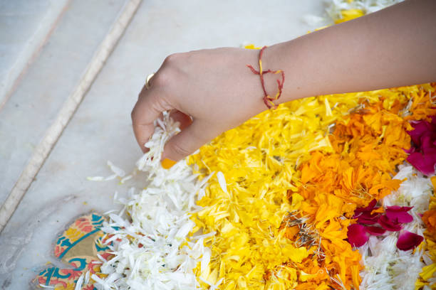 istock Indian woman dropping marigold jasmine flowers on a rangoli pattern on the floor while making a rangoli for diwali, new year or a wedding decoration as part of the hindu religion 1358417754