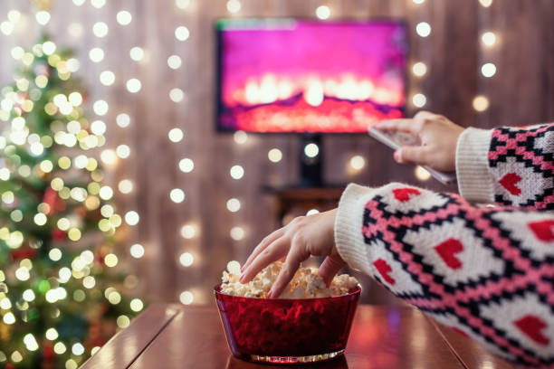 istock Christmas eve. Alone woman eating popcorn, watching tv, switching channels using remote control. Home cinema. Cropped, close up 1358418951