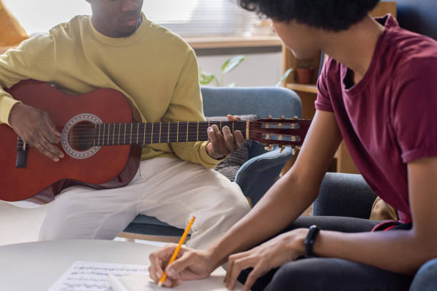 istock Young guy making notes and looking at music teacher playing guitar 1358422584
