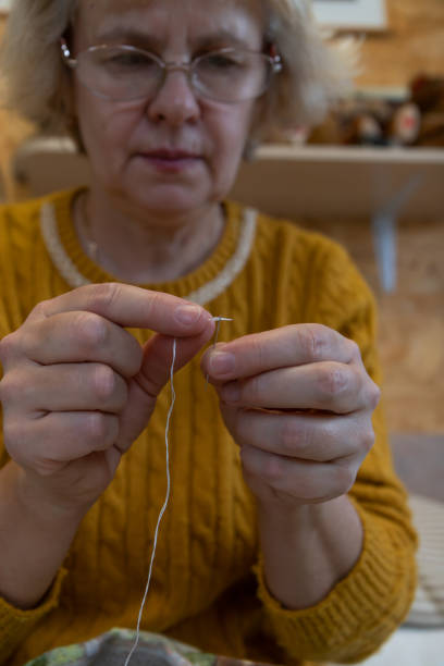 istock Middle-aged gray-haired woman wear glasses thread a needle. 1358425281