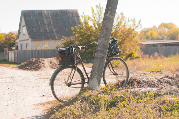 bicicleta usada antiga com duas cestas de aço ficam perto de um poste de concreto na vila. fundo rural - old obsolete antique old fashioned - fotografias e filmes do acervo