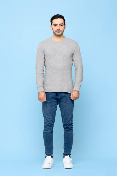 full length portrait of standing young handsome caucasian man looking at camera in isolated studio blue background - straight imagens e fotografias de stock