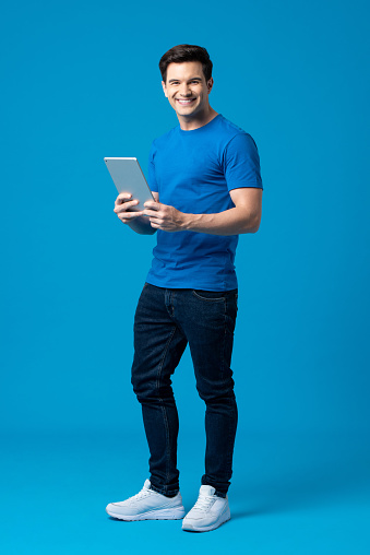 Full body portrait of happy Caucasian American man holding tablet computer isolated on blue studio background
