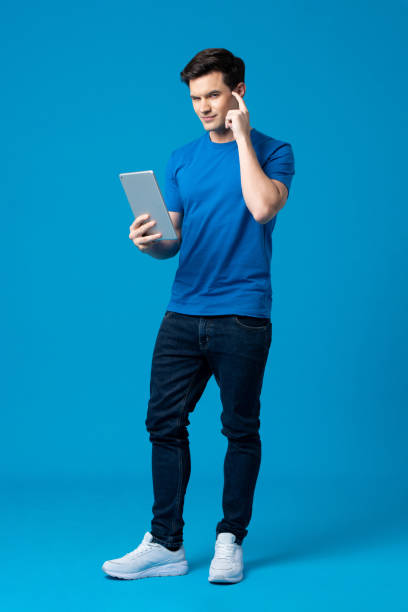 istock Young handsome Caucasian man holding tablet computer and pointing finger on head in isolated a light blue studio background 1358427477