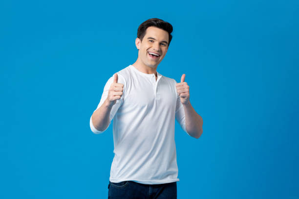 Young handsome Caucasian man giving thumbs up and smiling in light blue isolated background stock photo