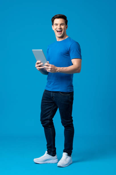 Surprise young handsome Caucasian man smiling and holding laptop computer in isolated light blue studio background stock photo