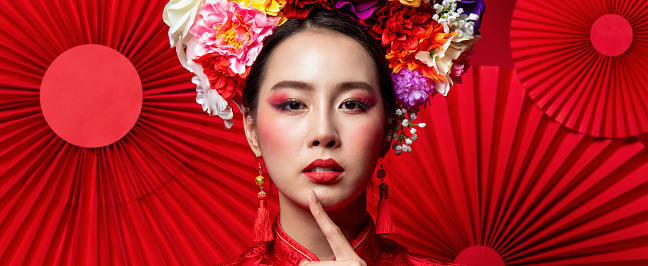 Gorgeous Asian woman in traditional with colorful make up and flower wreath on head in oriental style red fan banner background