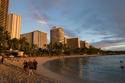 Oahu, USA - Nov 3, 2021: Tourists enjoying the beach as a rainbow form over Waikiki beach late in the day as a storm passes.