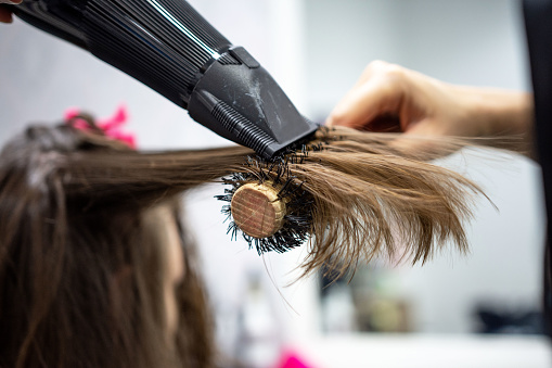 Professional woman hairdresser making hairstyle using hair dryer for young female in beauty salon