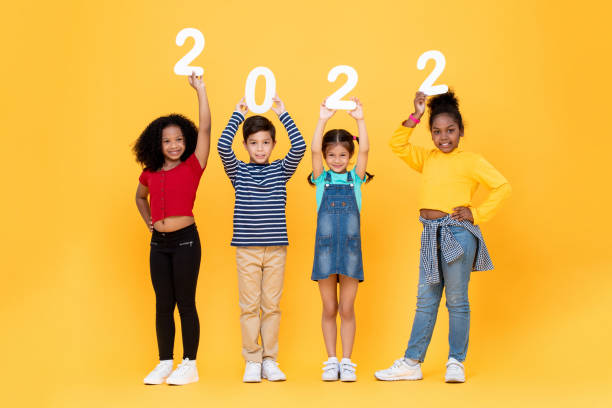 happy cute little kids smiling and holding 2022 numbers isolated on yellow studio background for new year concepts - pre adolescent child child group of people little boys imagens e fotografias de stock