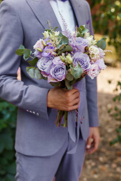 Groom in Very Peri suit holding in hands wedding bouquet, close-up. Man getting ready in the morning. Trendy color of the year 2022 in clothing Groom in Very Peri suit holding in hands wedding bouquet, close-up. Man getting ready in the morning. Trendy color of the year 2022 in clothing. dinner jacket stock pictures, royalty-free photos & images