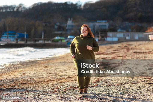 istock Overweight beautiful jogging at the seashore. Copy space. The concept of sport and activity 1358438597
