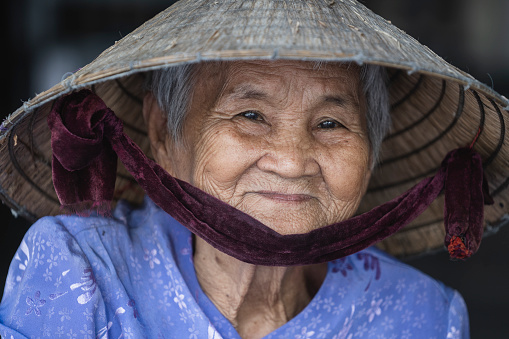 Nha Trang, Vietnam - March 30, 2020 : Ethnic happy old woman in straw hat on a street market of Nha Trang, Vietnam