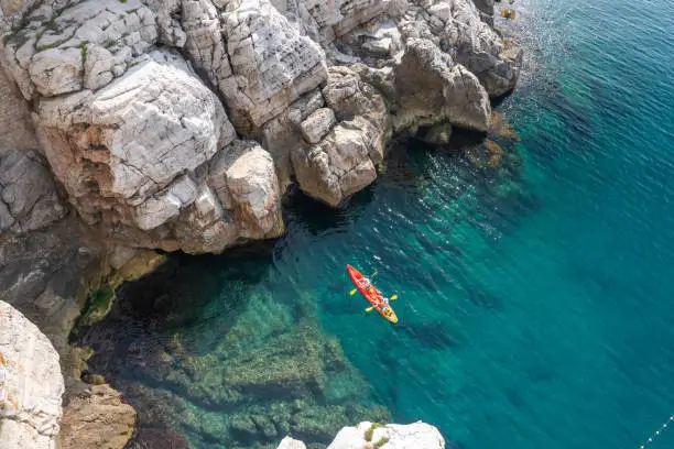 Photo of View from the rock cliffs of kayaker exploring the crystal clear Mediterranean waters of a cove off the coast of Dubrovnik, Croatia