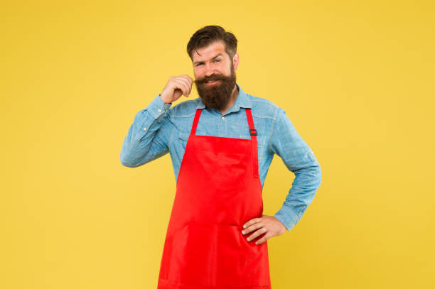 istock Preparation and culinary. mature bartender. his new business. guy in shop assistant uniform. smiling man with red apron on yellow background. Confident expression. Handsome male barista is working 1358442584