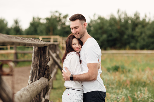 happy couple is hugging near wooden fence. young man and woman are having fun outdoors on a warm summer day