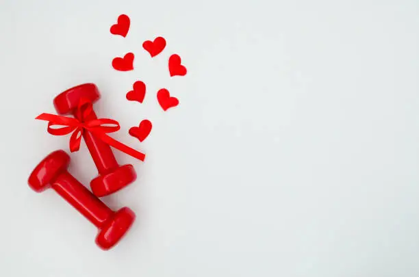 Photo of Two red dumbbells and hearts on a white background with copy space. Concept of Valentines day, healthy lifestyle, giving gifts, love of sports, shopping