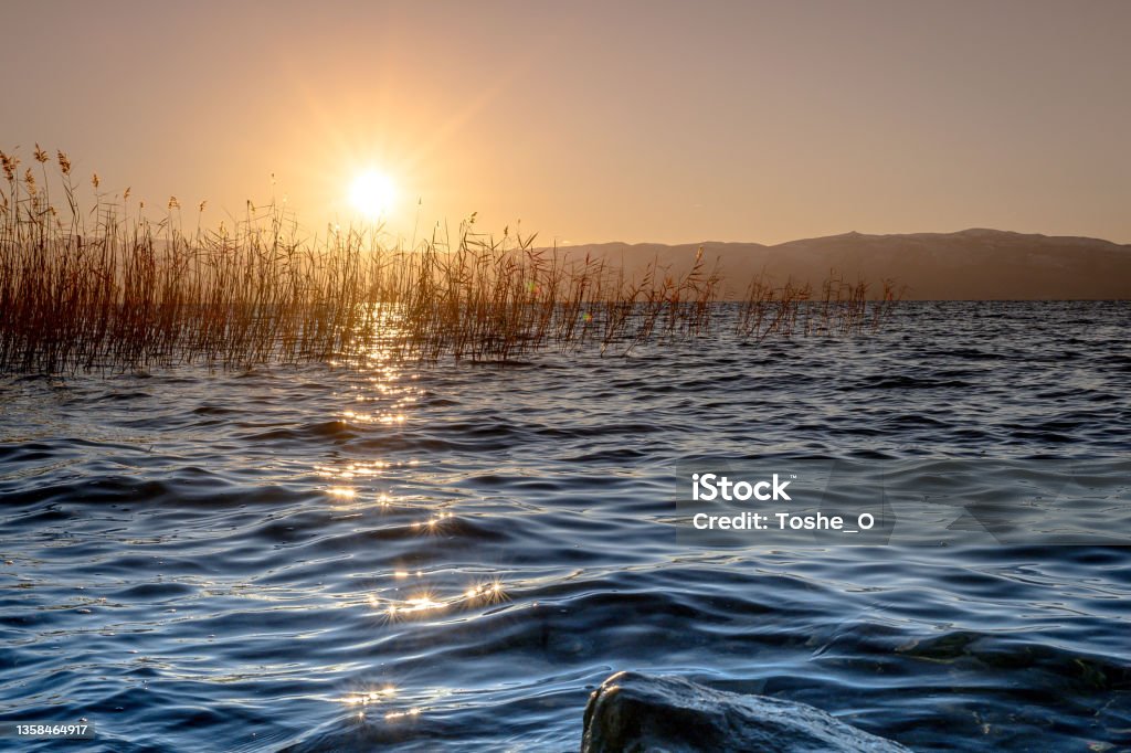 Beautiful sunset over a lake - environmental protection Beauty in nature with scenic view of a sunset over Ohrid lake in North Macedonia - with sunbeams going through lake reed Above Stock Photo