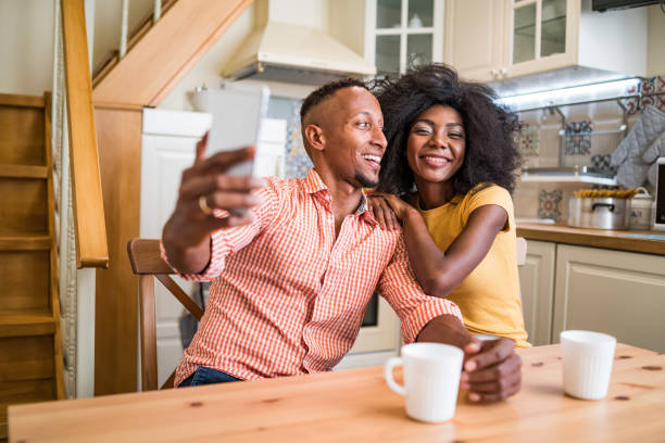 istock Young multiracial couple laughs while using smartphone - couple in love having breakfast together and making selfie picture with mobile phone 1358468540