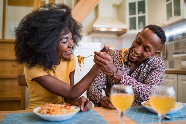 istock Shot of a young multiracial couple sharing spaghetti during a romantic dinner at a small living room 1358468564