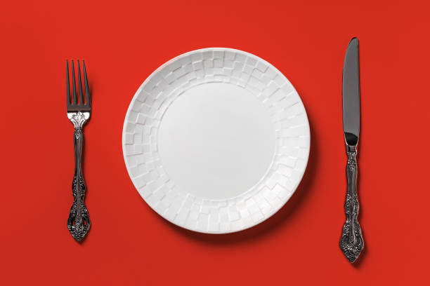 istock Empty white dinner plate, fork and table knife against red background. Blank mockup template for junk food, unhealthy eating, fast foods and bad eating habits concepts. 1358473167