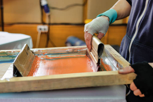 istock printing on t-shirts by silk screen method in a design studio. male hand with a squeegee. serigraphy production selective focus photo 1358475939
