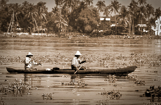Alappuzha, Kerala, India - circa oct 1975: two men paddle their canoe in the Backwater. Historical black and white photo.