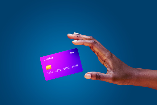 Close up african american female hand and levitating mockup bank credit card with online service on blue background. High quality photo