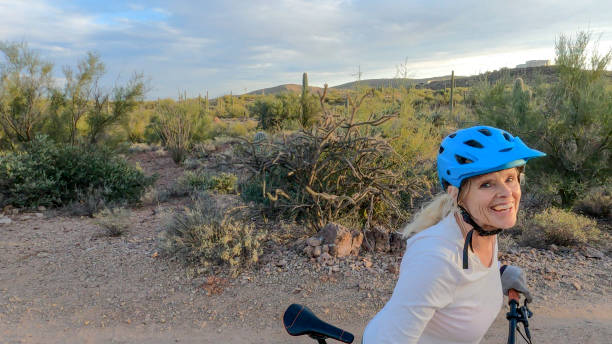 Female mountain biker follows trail, in desert Arid landscape surrounding long sleeved recreational pursuit horizontal looking at camera stock pictures, royalty-free photos & images