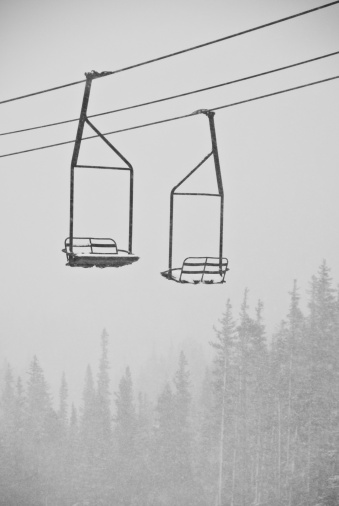An old style ski lift in a snow storm with trees in the background.