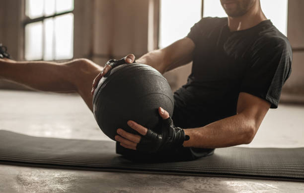 Man doing abs exercise with medicine ball Side view of crop unrecognizable athletic male doing side twist exercise with medicine ball during intense functional training in gym sportsman professional sport side view horizontal stock pictures, royalty-free photos & images