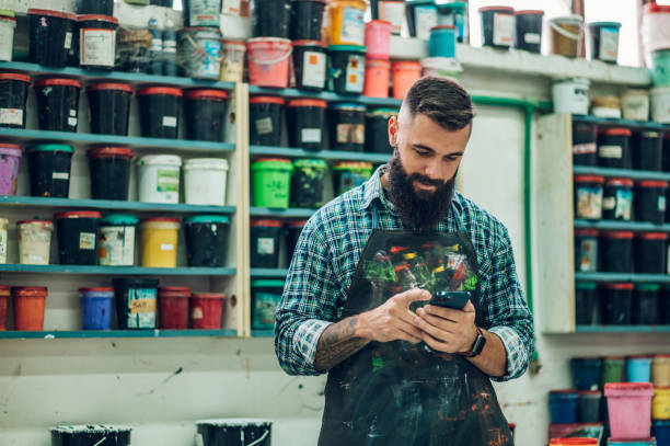 männlicher arbeiter mischt farben für den siebdruck in einer werkstatt und mit einem smartphone - silk screen fotos stock-fotos und bilder