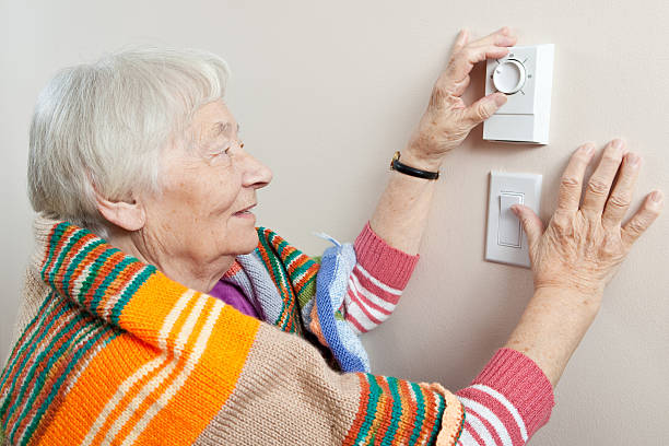 mulher idosa ajustar o termostato - energy saving fotos imagens e fotografias de stock