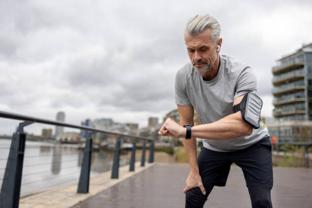 hombre mirando su reloj inteligente para rastrear su tiempo mientras corre al aire libre - men gray hair vitality healthy lifestyle fotografías e imágenes de stock