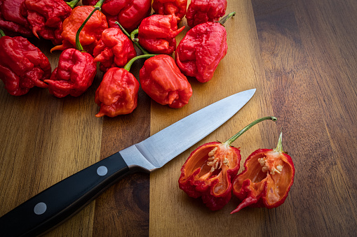 Photograph of Carolina Reaper Peppers on a wood countertop with knife - The hottest peppers in the world!