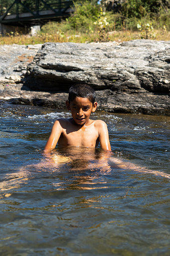 a young village boy playing in the river full of water on a bright sunny day