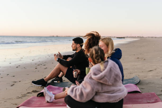 istock Multiethnic group of people sitting on a beach drinking tea during sunset 1358511884