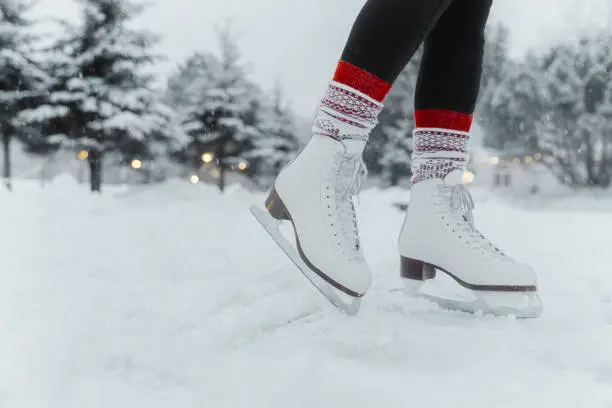 Figure skating woman skating on ice at outside rink during snowfall wearing female white leather boots. Family outdoor activity winter sport.