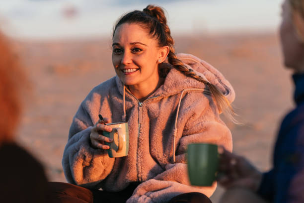 istock Woman drinking tea next to other people during sunset on a beach 1358513422