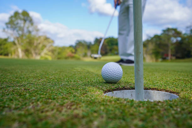 グリーンゴルフにボールを置くゴルファー、夕方に設定された太陽の上にレンズフレア。長いホールにゴルフボールを入れた後に勝つためにゴルファーのアクション - short game ストックフォトと画像
