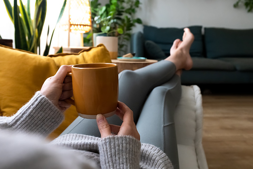 POV de una mujer joven relajándose en casa con una taza de café acostada en el sofá photo