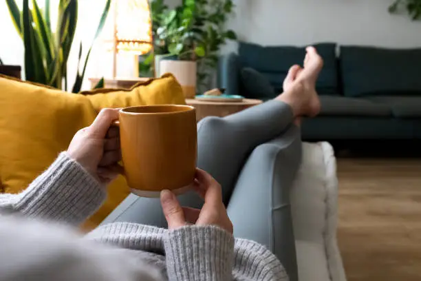 Photo of POV of young woman relaxing at home with cup of coffee lying on couch