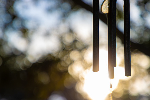 A traditional metal wind chime with the sun setting behind it. Selective focus, copy space on left. Peaceful photo.
