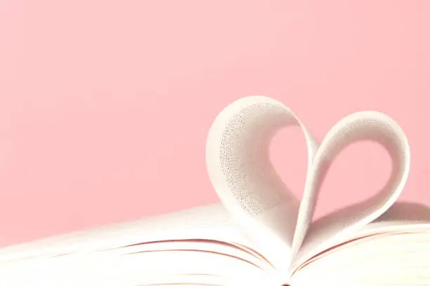 Photo of Book pages in shape of heart on pink background. Love, valentines or mother's day concept. Close up, copy space.