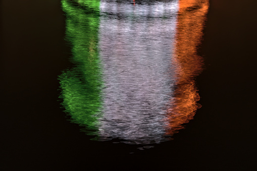 Beautiful closeup evening view of ring beam lighting of The Convention Centre Dublin reflecting in water and imitating Irish flag. Abstract