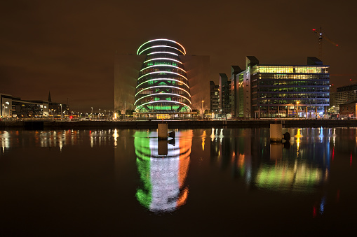 Dublin, Ireland - November 13, 2021: Beautiful wide angle evening view of The Convention Centre Dublin with ring beam lighting imitating Irish flag and reflection in water. Modern Dublin architecture